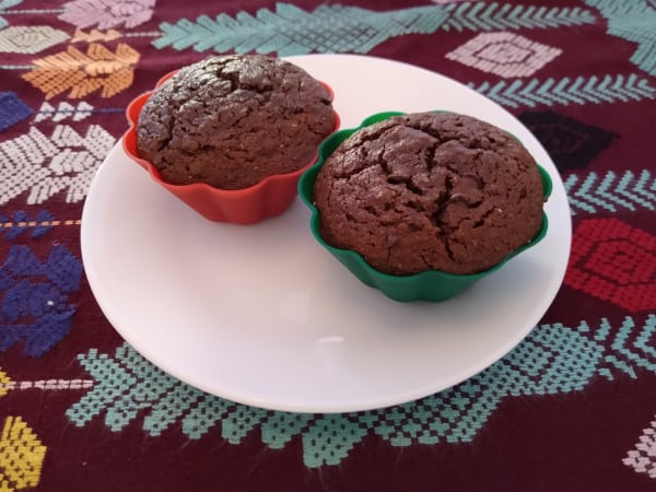 Gluten-Free Coconut Chocolate Mint Muffins from Gluten-Free & Paleo Travels. Two muffins in silicone baking cups on a white plate on top of a colorful tablecloth.