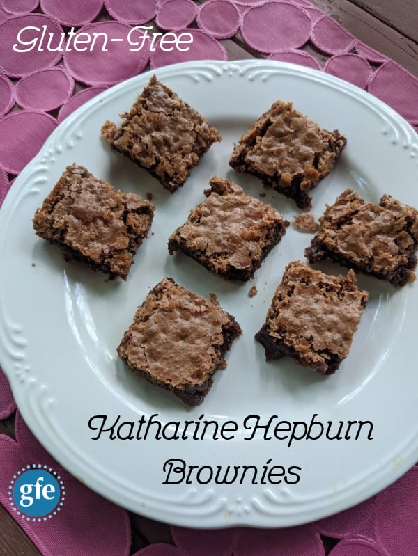 Brownies Katharine Hepburn senza glutine tagliati a quadrati diagonali su un piatto bianco su uno sfondo con motivi rosa.