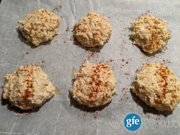Perfect Gluten-Free Crab Cakes with Old Bay Seasoning and a sprinkle of smoked paprika before going in the oven. Six crab cakes on parchment-lined baking sheet ready to go in the oven.