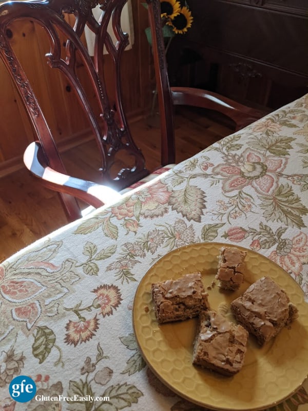 Gluten-Free Chewy Pecan Squares. Plate of four on dining room table with Fall linen tablecloth and dining room chair.