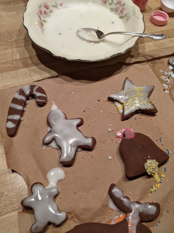 Frosted and Decorated Gluten-Free Chocolate Gingerbread Cookies drying on paper bag beside bowl of frosting.