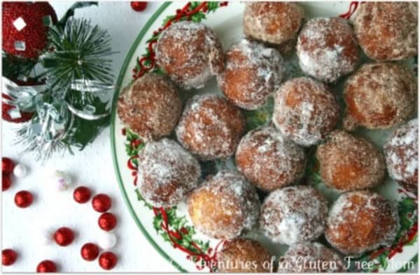 Sweet Gluten-Free Fritters (aka Förtchen, Futtjens, or Ferdons) dusted in granulated sugar and placed side by side on a Christmas plate with a decorative garland and other decorations to the side.