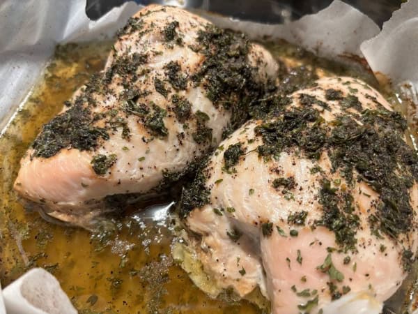 Two Zesty Turkey Breast Tenderloins resting side by side in baking juices in parchment-lined baking dish after baking and before slicing.
