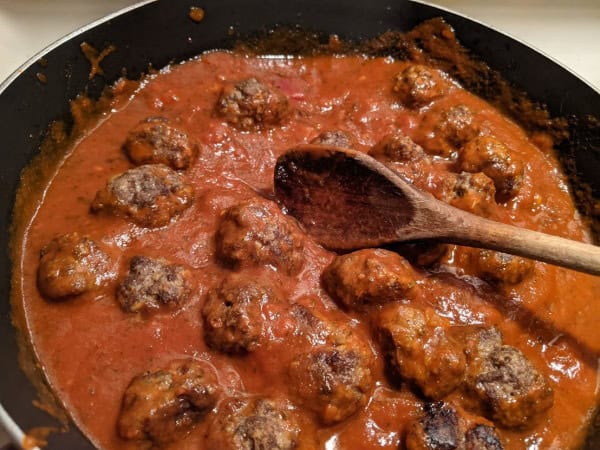 Easy Gluten-Free Italian Meatballs simmering in marinara sauce in non-stick skillet with wooden spoon sitting in the middle of the skillet..