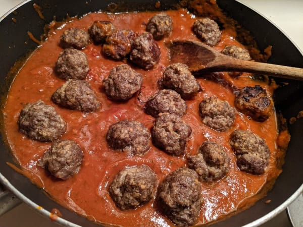 Easy Gluten-Free Italian Meatballs simmering with marinara sauce in non-stick skillet with wooden spoon resting off to the side.