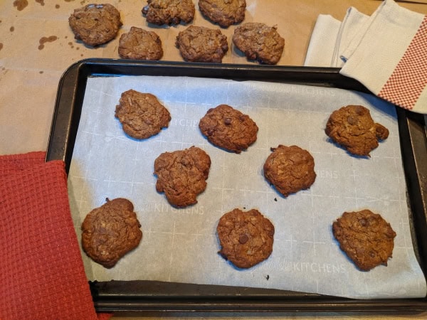 Flourless Gluten-Free Cashew Butter Coconut Chocolate Chip Cookies. Some cookies already cooling on brown paper and other cookies still on the parchment-lined baking sheet nestled in two dish towels.