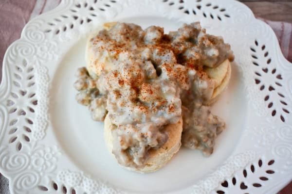 Gluten-free biscuits and sausage gravy on a white embellished and cut out dinner plate on a red and white dish towel.