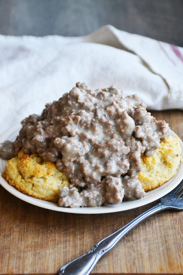 Gluten-Free Biscuits and Beef Sausage Gravy from Raia's Recipes on a white plate trimmed in blue with a fork and red and white striped dish towel nearby.