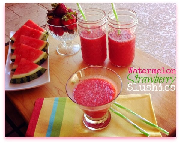 Watermelon-Strawberry Slushies in glasses beside a plate of watermelon slices and a bowl of strawberries on a colorful striped placemat.