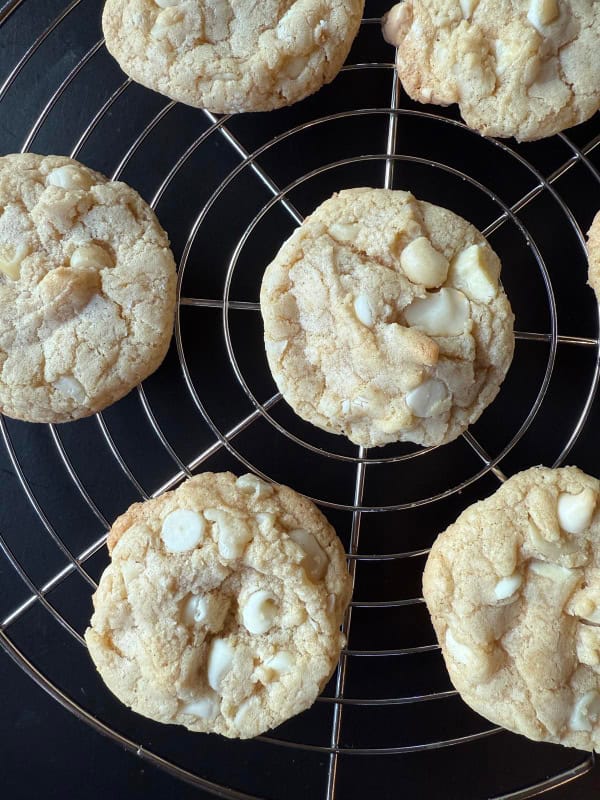 Gluten-Free White Chocolate Macadamia Nut Cookies from Lynn's Kitchen Adventures spread on a circular cooling rack over a black surface.