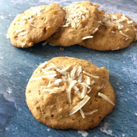 Tipsy Tropical Treats: Cookies with Pineapple, Mango, Coconut, Macadamias, and Rum from In Johnna's Kitchen on a slate surface with one in front and three stacked like dominoes in the back.