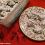 Naturally gluten-free Forgotten Cookies nestled in green plastic wrap in a Tupperware bread container sitting on a holiday tablecloth.